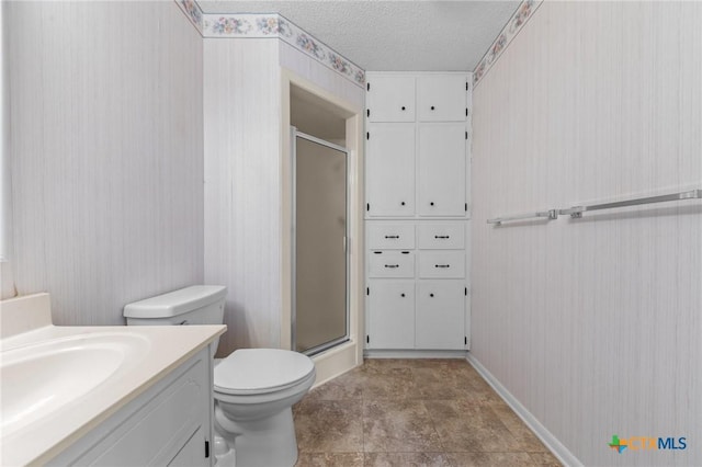 bathroom featuring a stall shower, vanity, a textured ceiling, toilet, and baseboards