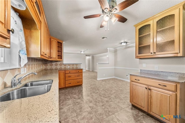 kitchen with a sink, decorative backsplash, a ceiling fan, light stone countertops, and open floor plan