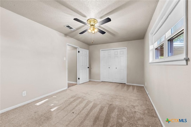 unfurnished bedroom featuring carpet flooring, a textured ceiling, baseboards, a closet, and a ceiling fan
