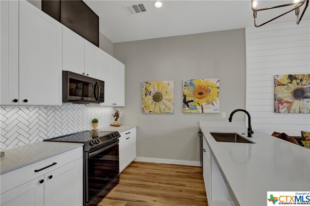 kitchen with light wood-type flooring, black / electric stove, sink, and white cabinetry