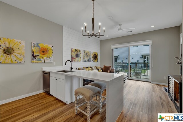 kitchen with white cabinetry, sink, a kitchen breakfast bar, hanging light fixtures, and light wood-type flooring