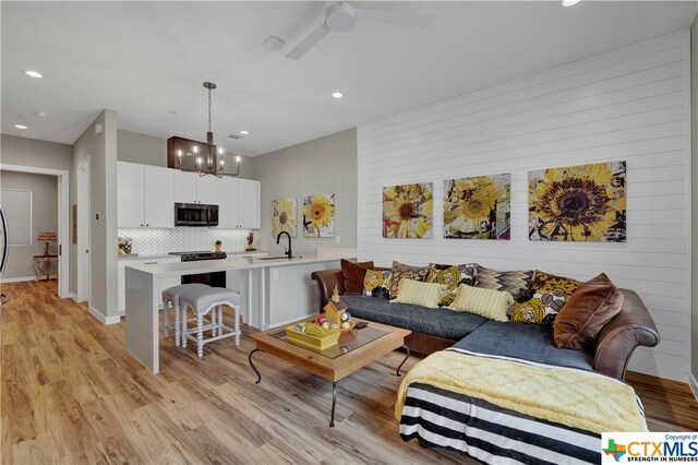 living room with wood walls, a chandelier, sink, and light wood-type flooring