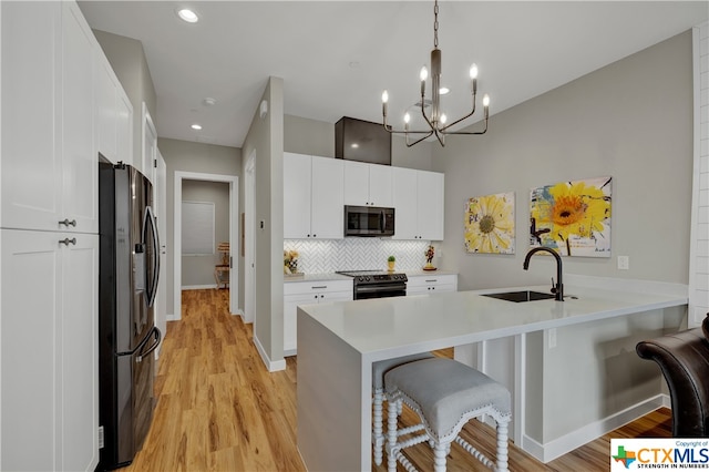 kitchen featuring light hardwood / wood-style floors, white cabinetry, appliances with stainless steel finishes, a breakfast bar area, and hanging light fixtures