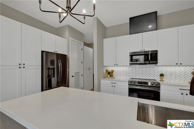 kitchen featuring backsplash, appliances with stainless steel finishes, hanging light fixtures, white cabinets, and a chandelier