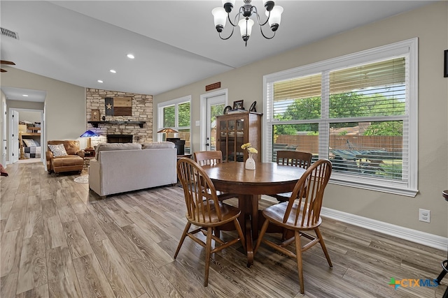 dining room featuring a stone fireplace, light wood-type flooring, vaulted ceiling, and ceiling fan with notable chandelier