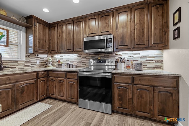 kitchen with light stone countertops, appliances with stainless steel finishes, backsplash, and light hardwood / wood-style flooring