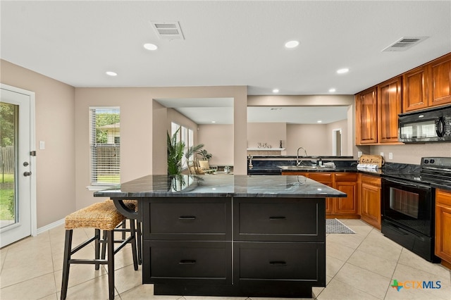 kitchen with a kitchen breakfast bar, black appliances, a center island, and dark stone countertops