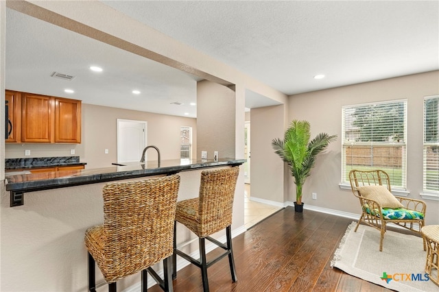 kitchen with kitchen peninsula, a breakfast bar area, a textured ceiling, and dark hardwood / wood-style flooring