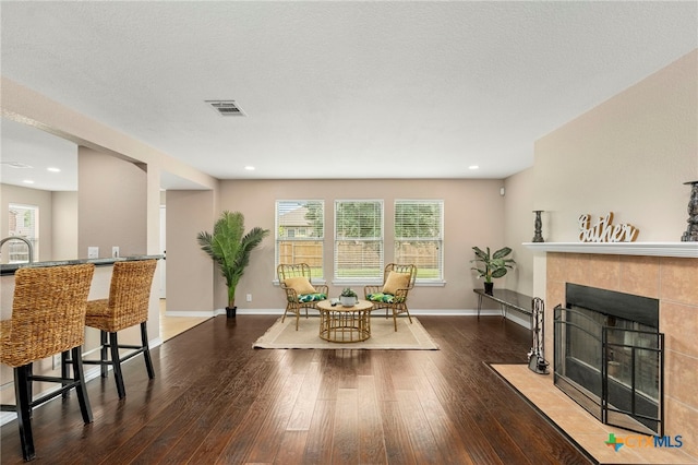 living room with a tiled fireplace, dark hardwood / wood-style flooring, and a textured ceiling