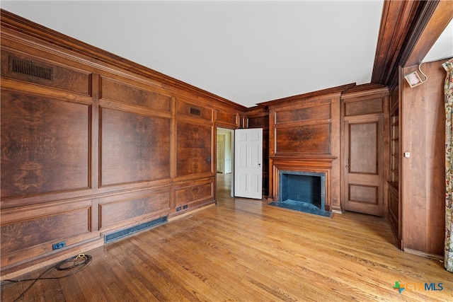 unfurnished living room featuring wooden walls, light hardwood / wood-style floors, and crown molding