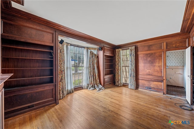 unfurnished office with built in shelves, light wood-type flooring, wooden walls, and ornamental molding