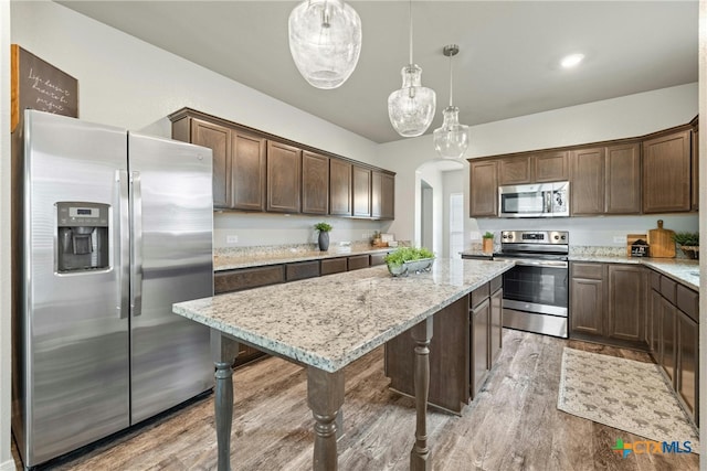 kitchen featuring dark brown cabinets, hanging light fixtures, appliances with stainless steel finishes, and light hardwood / wood-style flooring