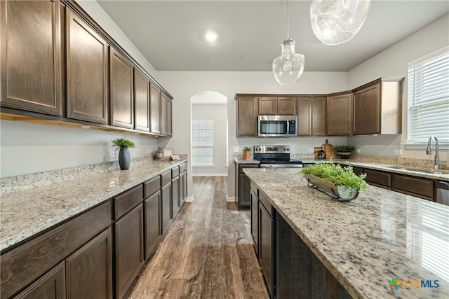 kitchen with dark brown cabinetry, sink, hanging light fixtures, stainless steel appliances, and dark hardwood / wood-style floors