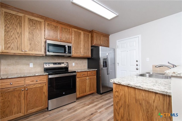 kitchen featuring decorative backsplash, appliances with stainless steel finishes, light stone countertops, sink, and light hardwood / wood-style flooring