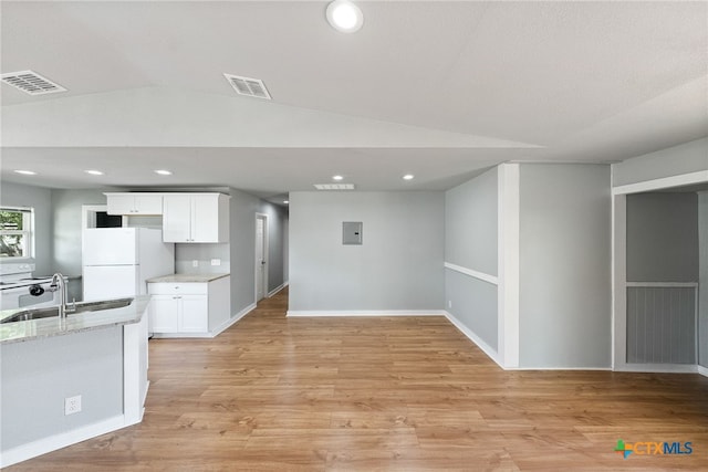 kitchen featuring light stone counters, light hardwood / wood-style flooring, white cabinets, white fridge, and vaulted ceiling