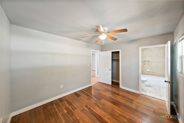 unfurnished bedroom with dark wood-type flooring, ceiling fan, ensuite bath, and a closet