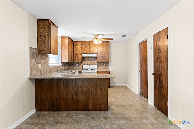 kitchen with white gas range oven, a sink, backsplash, ceiling fan, and under cabinet range hood
