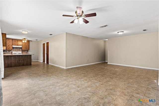 unfurnished living room with baseboards, a ceiling fan, and visible vents
