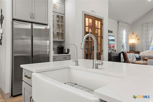 kitchen with gray cabinets, stainless steel refrigerator, lofted ceiling, sink, and light stone counters