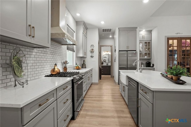 kitchen featuring light hardwood / wood-style flooring, gray cabinets, appliances with stainless steel finishes, backsplash, and wall chimney exhaust hood