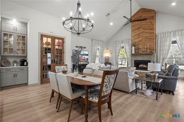 dining space with high vaulted ceiling, a stone fireplace, a wealth of natural light, and light wood-type flooring