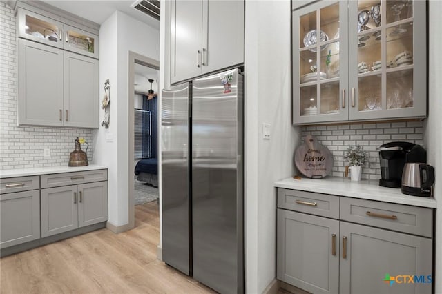 kitchen with tasteful backsplash, light wood-type flooring, gray cabinetry, and stainless steel refrigerator