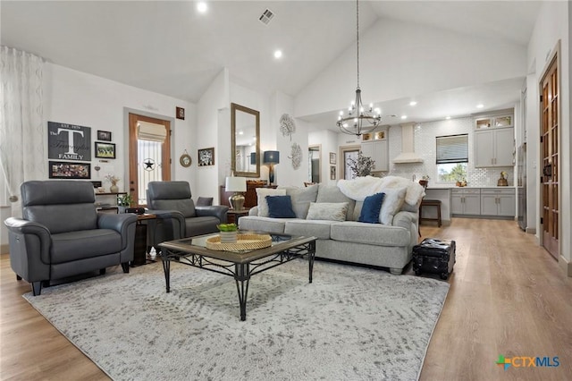 living room featuring an inviting chandelier, plenty of natural light, high vaulted ceiling, and light hardwood / wood-style flooring