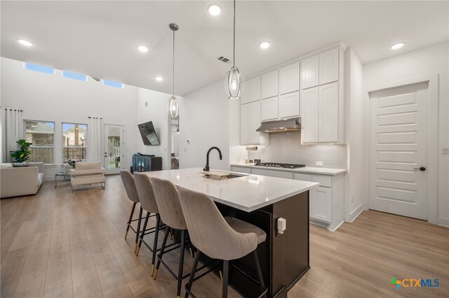 kitchen with white cabinets, light wood-type flooring, sink, and an island with sink