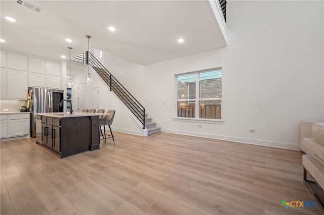 kitchen featuring white cabinetry, hanging light fixtures, light hardwood / wood-style floors, a kitchen bar, and a kitchen island with sink