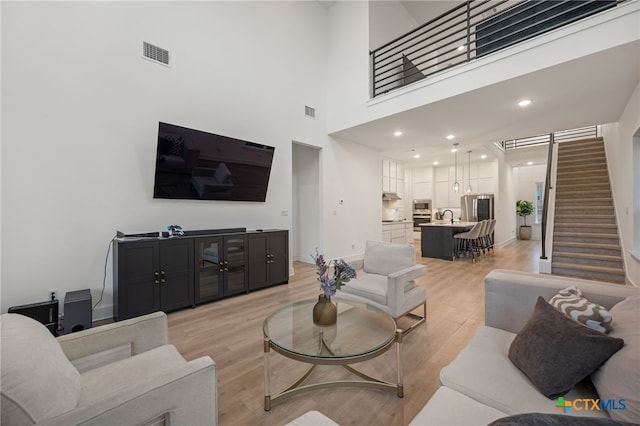 living room with a towering ceiling, sink, and light hardwood / wood-style flooring