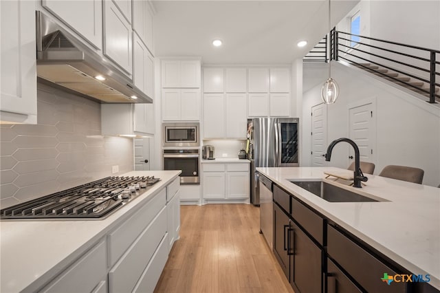 kitchen with stainless steel appliances, sink, pendant lighting, light hardwood / wood-style flooring, and white cabinetry