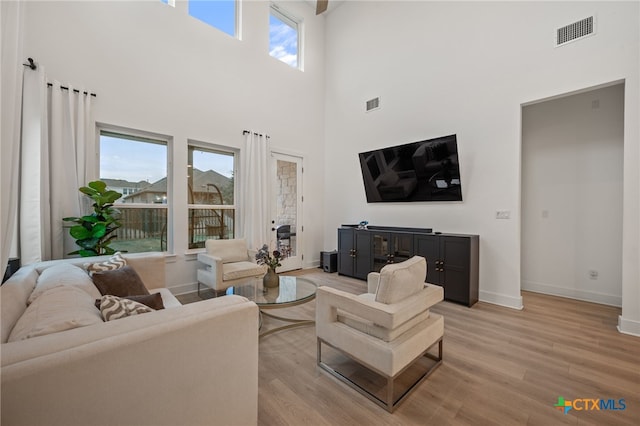 living room featuring a towering ceiling, light wood-type flooring, and plenty of natural light