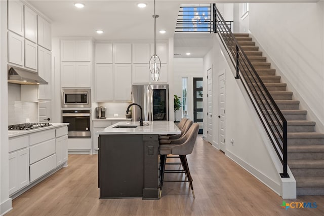 kitchen featuring hanging light fixtures, sink, an island with sink, appliances with stainless steel finishes, and white cabinetry