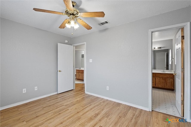 unfurnished bedroom featuring light wood-type flooring, ensuite bathroom, ceiling fan, and sink