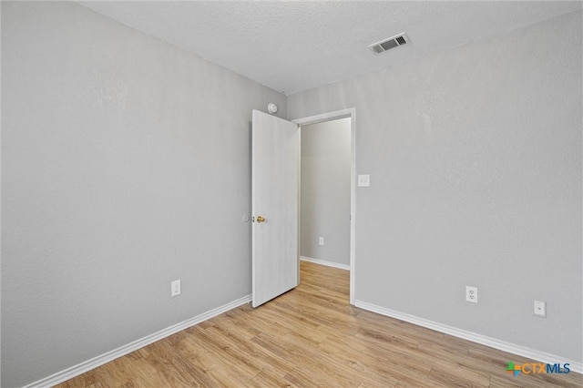 spare room with light wood-type flooring and a textured ceiling