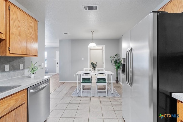 kitchen with pendant lighting, backsplash, a textured ceiling, appliances with stainless steel finishes, and light tile patterned flooring