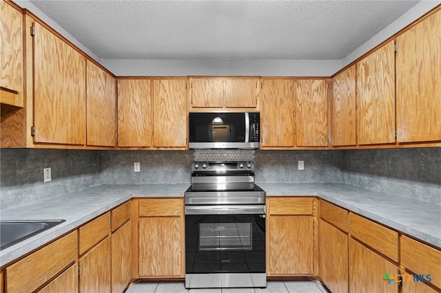 kitchen with backsplash, sink, a textured ceiling, light tile patterned flooring, and stainless steel appliances