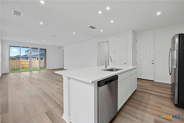 kitchen featuring white cabinetry, sink, stainless steel appliances, light hardwood / wood-style flooring, and a center island with sink