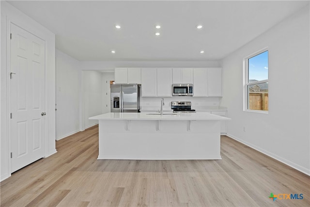 kitchen with white cabinets, light hardwood / wood-style flooring, an island with sink, and stainless steel appliances