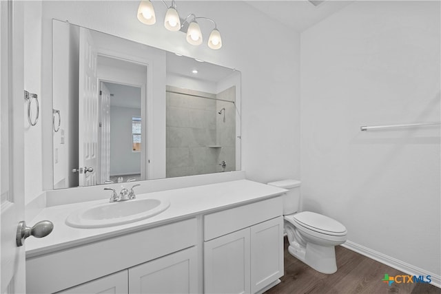 bathroom with toilet, a tile shower, wood-type flooring, and vanity