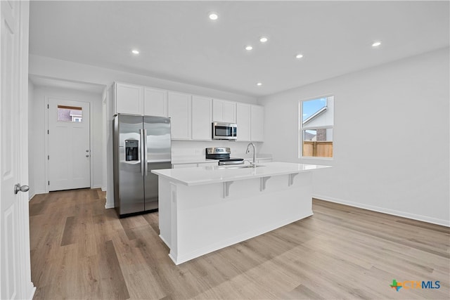 kitchen featuring a breakfast bar, a center island with sink, light hardwood / wood-style flooring, appliances with stainless steel finishes, and white cabinetry