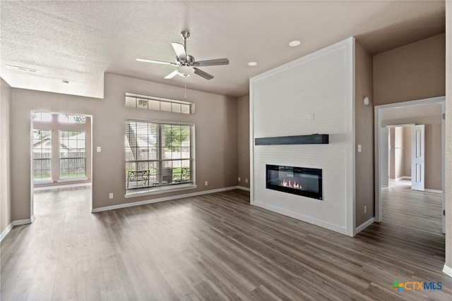 unfurnished living room with baseboards, ceiling fan, wood finished floors, and a large fireplace