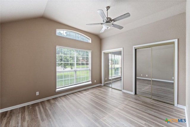 unfurnished bedroom with two closets, baseboards, wood finished floors, and lofted ceiling