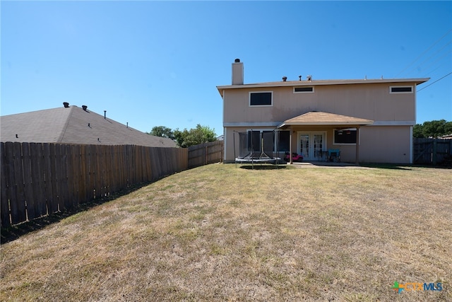 back of house featuring a patio area, a lawn, and a trampoline