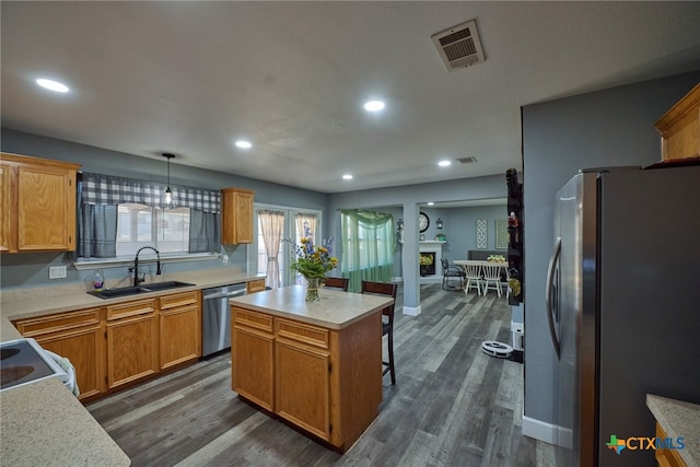 kitchen featuring stainless steel appliances, sink, a kitchen island, dark wood-type flooring, and pendant lighting