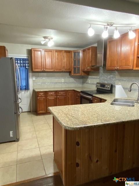 kitchen featuring brown cabinetry, stainless steel appliances, wall chimney range hood, a sink, and a peninsula