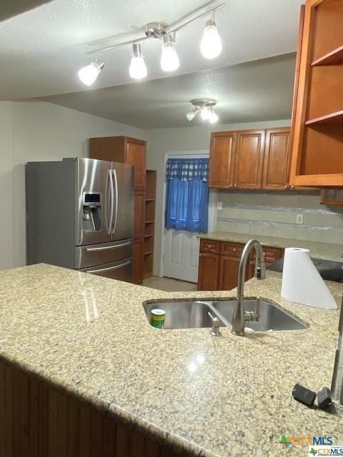 kitchen with light stone countertops, stainless steel refrigerator with ice dispenser, brown cabinets, and a sink