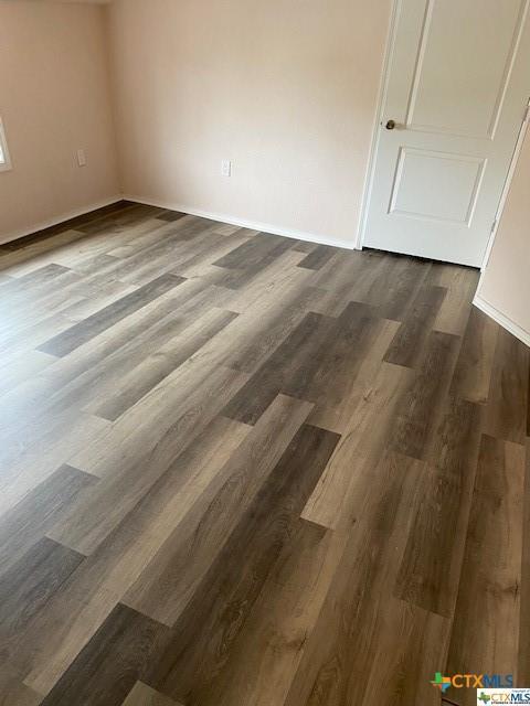 unfurnished room featuring baseboards and dark wood-type flooring