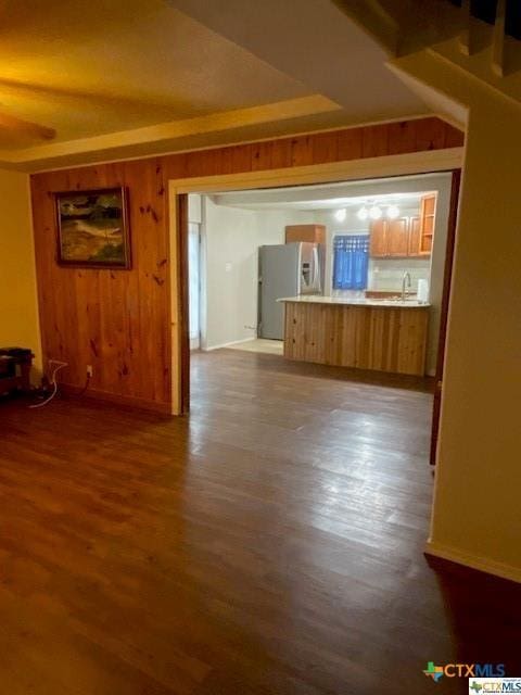 unfurnished living room featuring dark wood-style flooring, wood walls, and baseboards