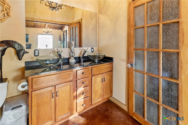 bathroom with toilet, vanity, concrete floors, and a notable chandelier